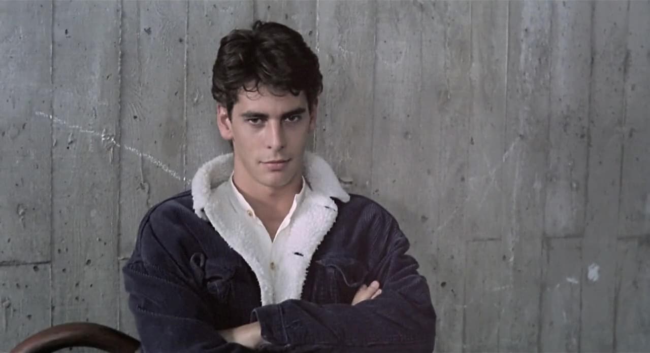 Fotograma de la película Tesis (1996) con un joven Eduardo Noriega apoyado en una pared, vistiendo la cazadora con cuello de borreguito y camisa blanca que después se recreó en la fotografía actual del hero.