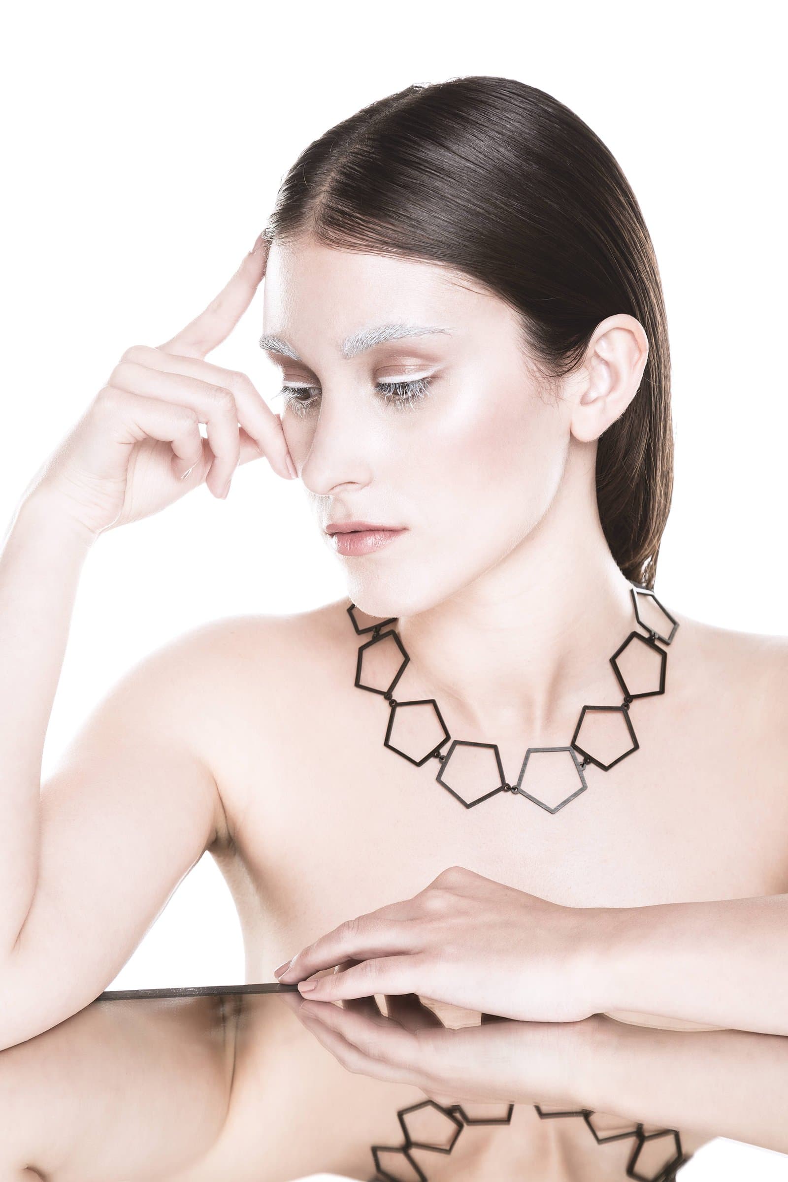 Alicia con un collar geométrico como pieza protagonista, maquillaje high-key y reflejo en espejo, fotografía publicitaria de joyería