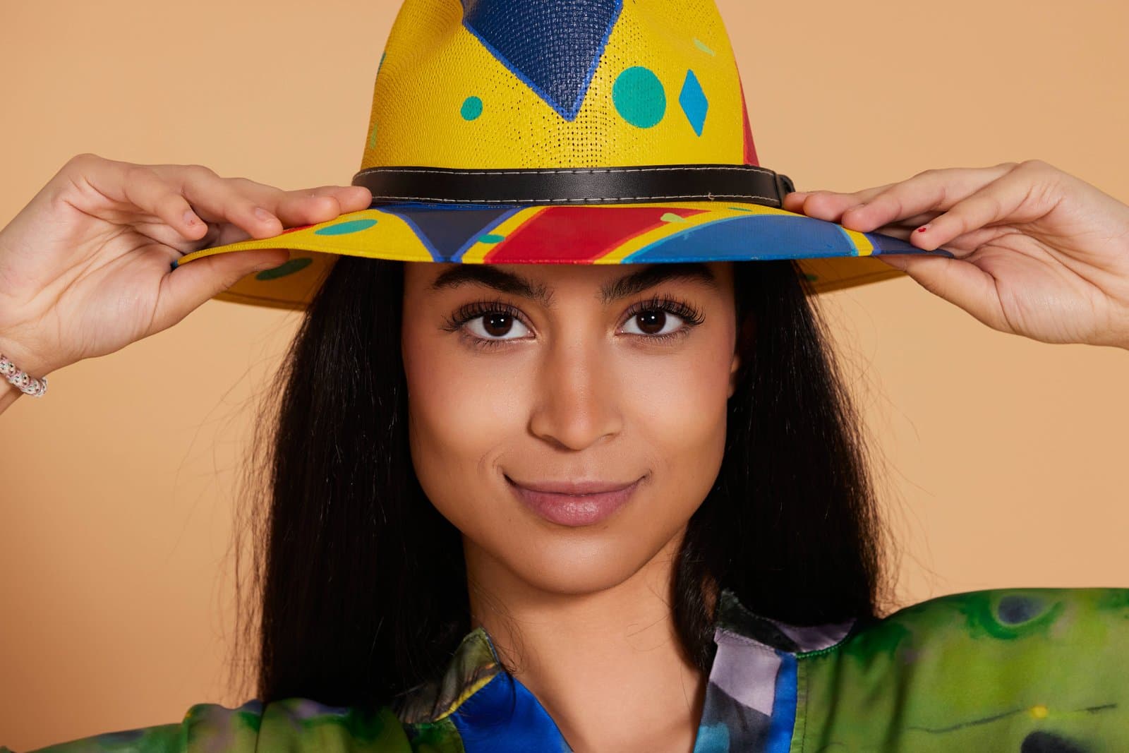 Keisi Ruiz sujetando con ambas manos un sombrero pintado a mano de colores, fotografía publicitaria para Aires del Arte