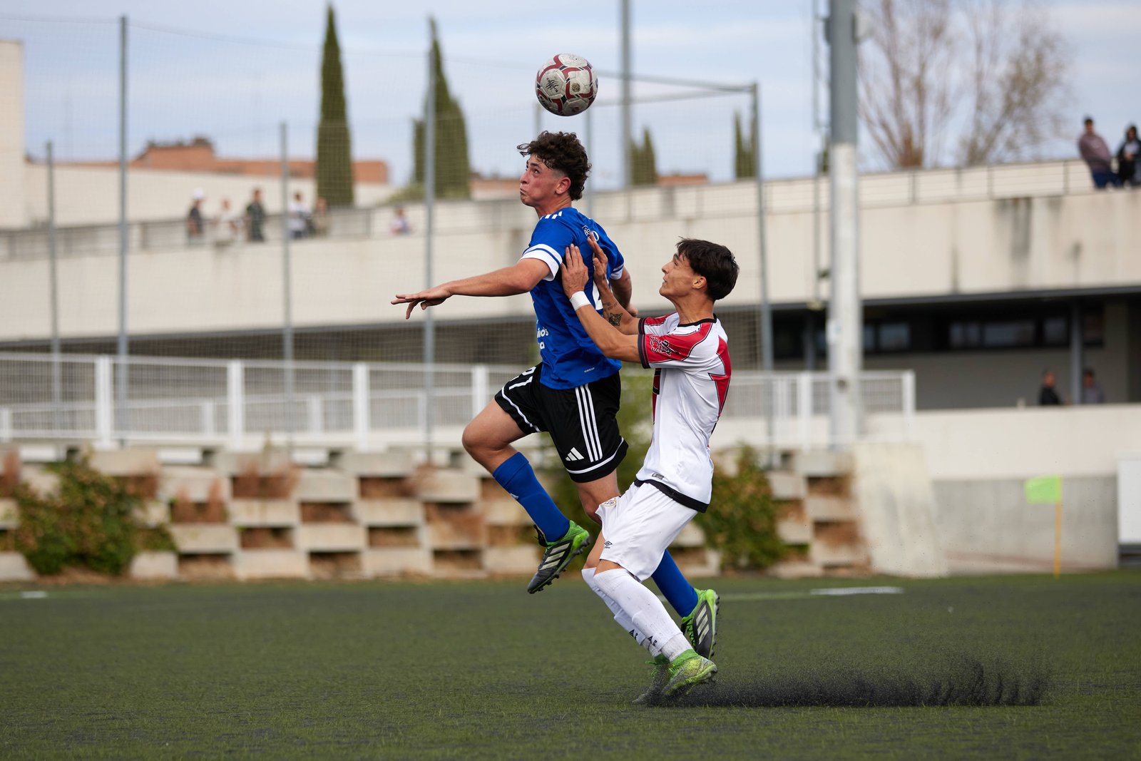 Defensa central del Juvenil de Las Rozas despeja de cabeza ante el Rayo Vallecano en el área propia.